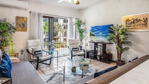 A living room with a glass coffee table, two armchairs, a sofa, a ceiling fan, and a large window with curtains. - Cozy Apartment w/ Balcony, Pool Views, Free Wifi (Puerto Vallarta)