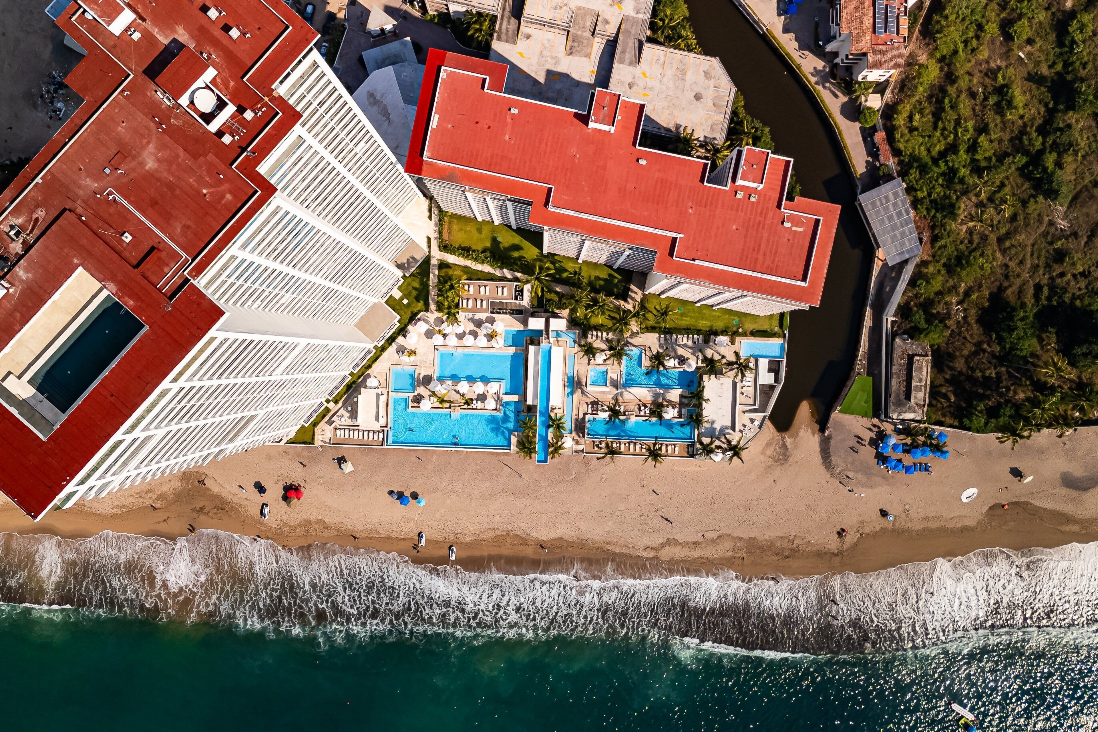 Luftaufnahme eines Küstenhotels mit Dachpool, Strand und Meerblick.
