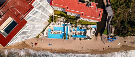 Luftaufnahme eines Küstenhotels mit Dachpool, Strand und Meerblick.