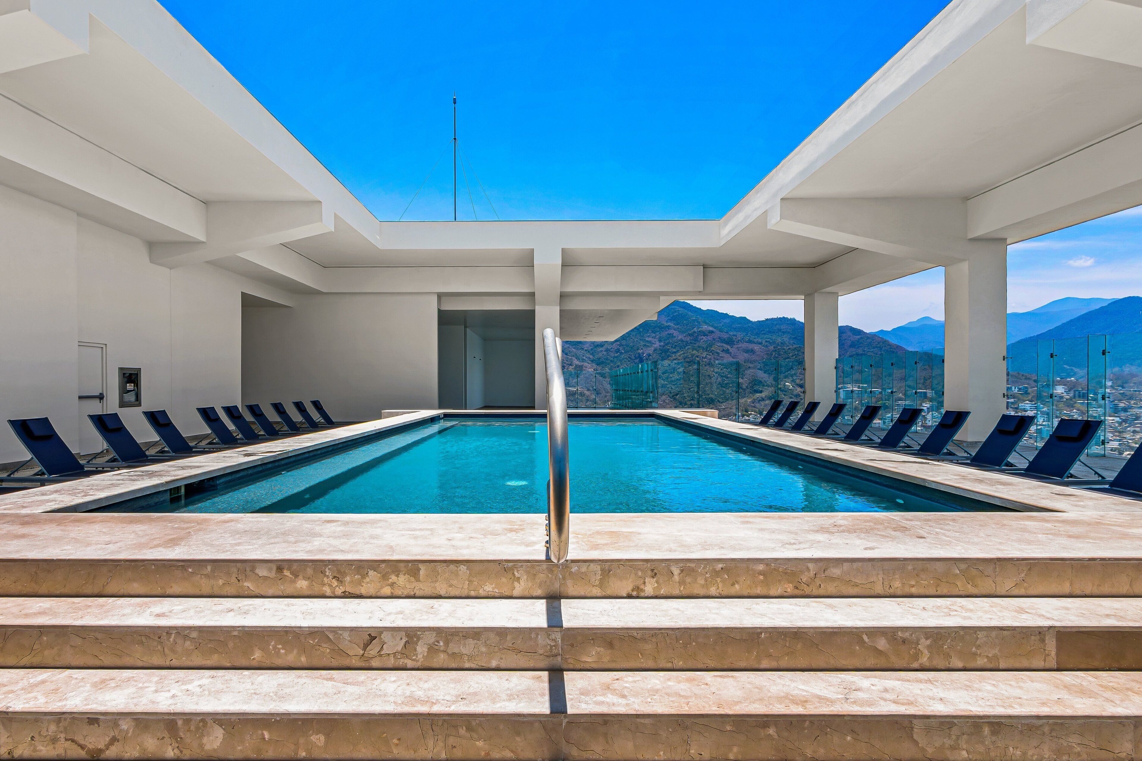 A swimming pool with steps leading up to it, surrounded by lounge chairs, and a view of mountains in the background.