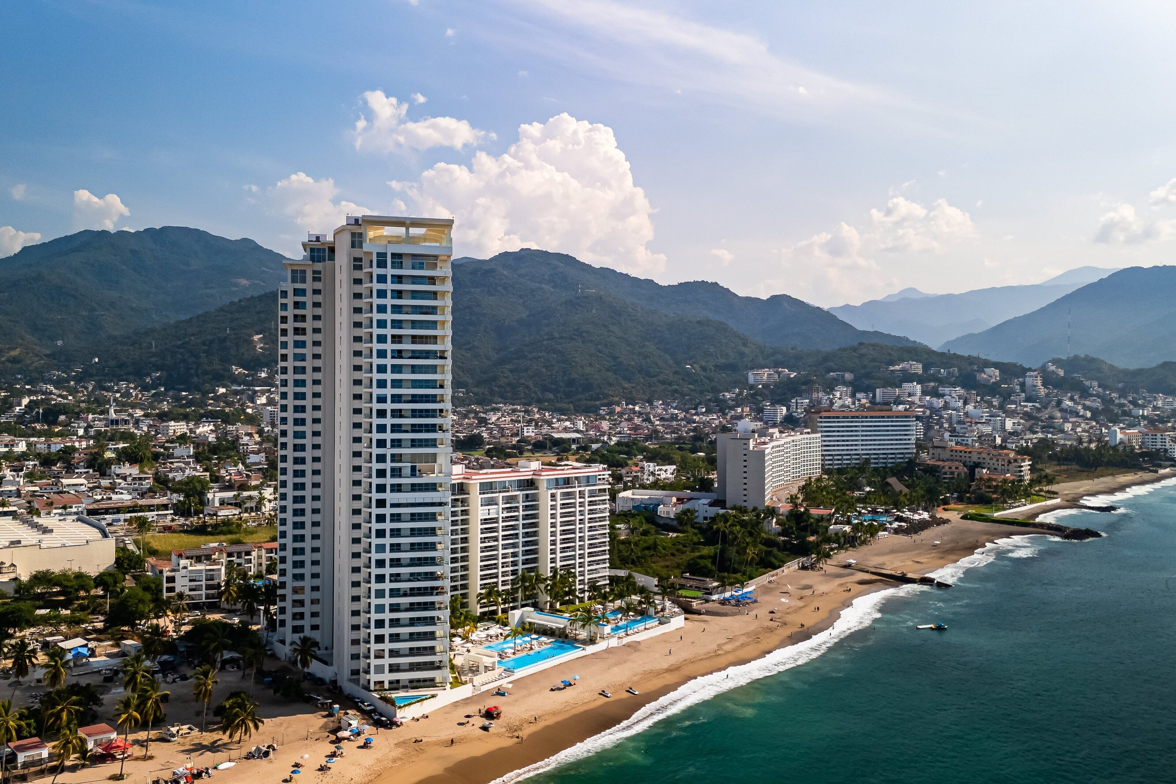 A high-rise hotel with a beach view, a pool, and a beach area with umbrellas.