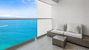 A balcony with a view of the ocean, a wicker sofa with cushions, and a small table. - Stylish Oceanfront Condo With Infinity Pool, Rooftop Deck & Beach Access (Puerto Vallarta)