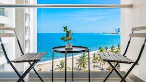 A balcony with a view of the ocean and palm trees. - Modern Oceanfront Studio With Breathtaking Sunsets, Heated Pools & Beach Access (Puerto Vallarta)