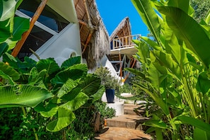 A tropical resort with a thatched-roof structure, a white exterior, and lush greenery.
