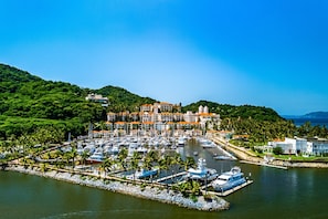 A marina with boats, a building with multiple floors, and a hilly backdrop.