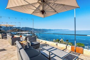 A rooftop terrace with outdoor seating, a large umbrella, and a view of the ocean. - Luxurious Partial Ocean-view Suite With 3 Pools, hot Tub, gym & Balcony (Puerto Vallarta)