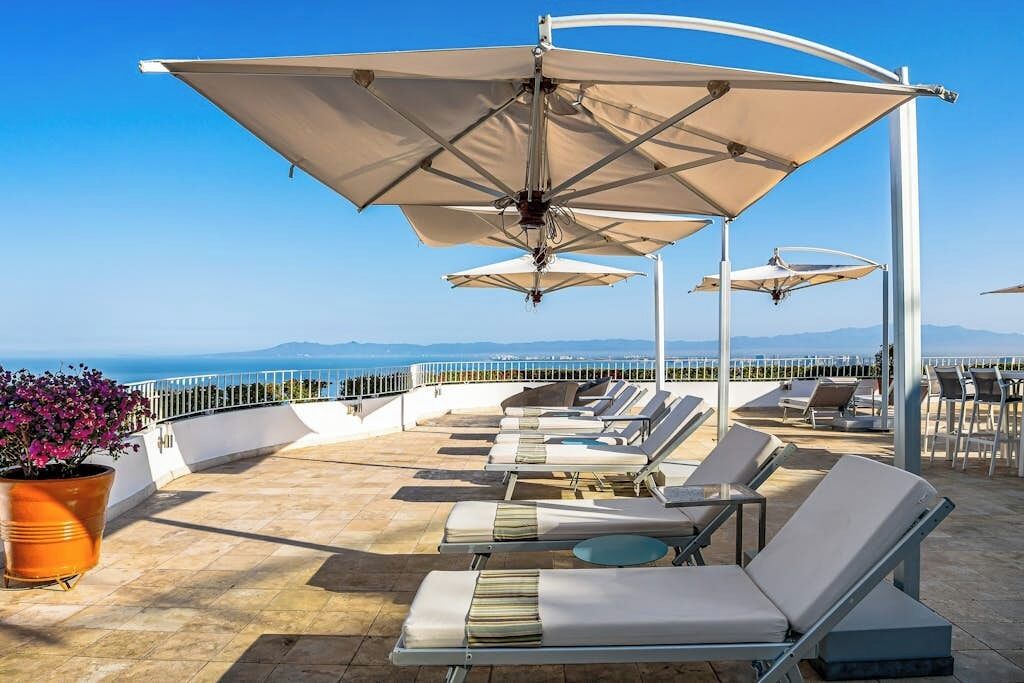 A rooftop terrace with sun loungers, umbrellas, and a view of the sea.