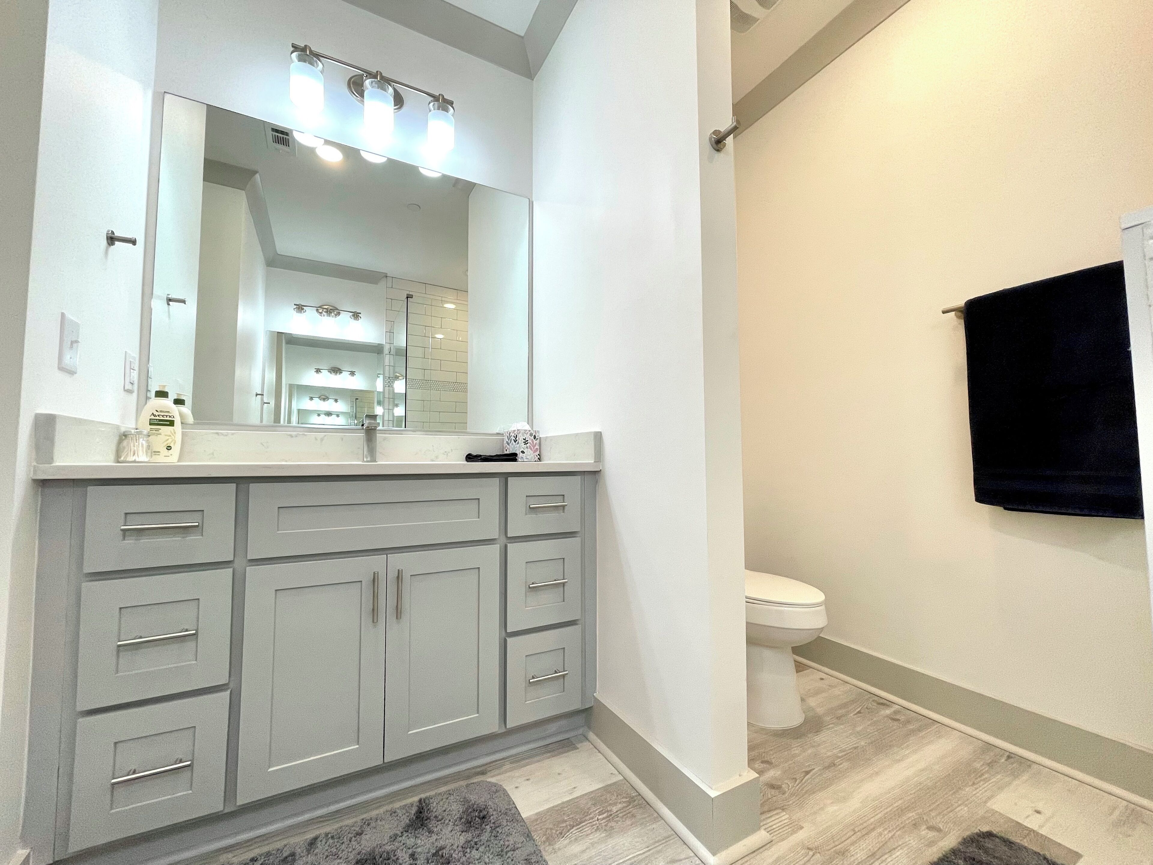 A modern bathroom with a large vanity, a toilet, and a mirror with lights.