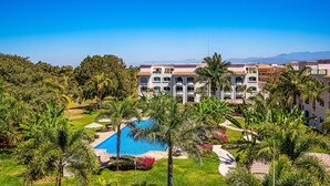 A resort with a swimming pool, palm trees, and a large building with multiple balconies. - Cozy Condo With Loft, Private Balcony and Gorgeous Shared Pool (Nuevo Nayarit)