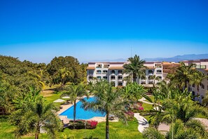 A resort with a swimming pool, palm trees, and a large building with multiple balconies. - Cozy Condo With Loft, Private Balcony and Gorgeous Shared Pool (Nuevo Nayarit)