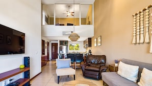 A modern living room with a sofa, chairs, a coffee table, a TV, and a dining area in the background. - Cozy Condo With Loft, Private Balcony and Gorgeous Shared Pool (Nuevo Nayarit)