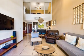 A modern living room with a sofa, chairs, a coffee table, a TV, and a dining area in the background. - Cozy Condo With Loft, Private Balcony and Gorgeous Shared Pool (Nuevo Nayarit)
