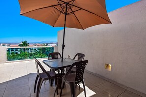 A patio with a table and chairs, an umbrella, and a view of buildings and greenery. - Cozy Condo With Loft, Private Balcony and Gorgeous Shared Pool (Nuevo Nayarit)