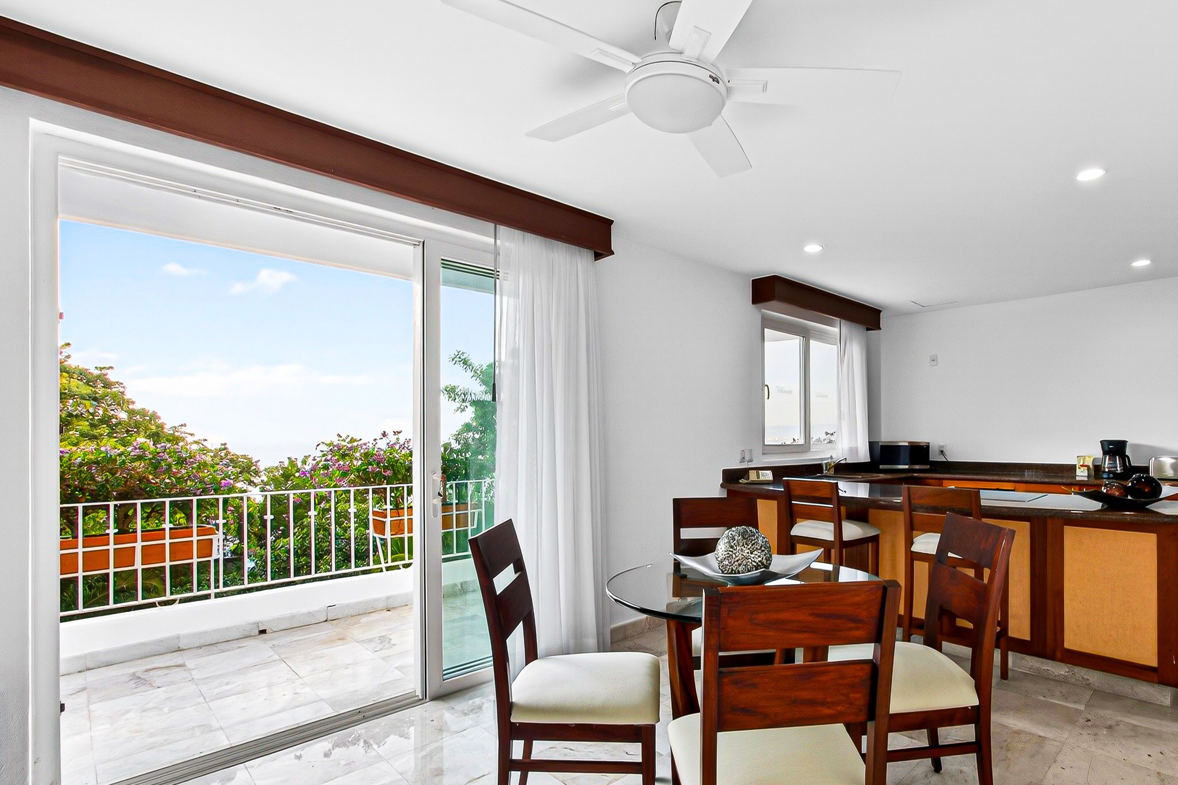 Una cocina moderna con comedor, ventilador de techo y vistas a un balcón con mobiliario exterior.