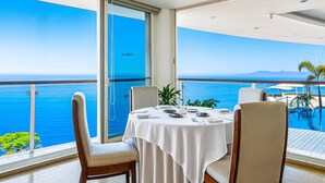 A dining area with a table set for four, overlooking a body of water and a distant mountain range. - Spacious Suite With Wraparound Terrace, Rooftop Infinity Pool & Resort Amenities (Puerto Vallarta)