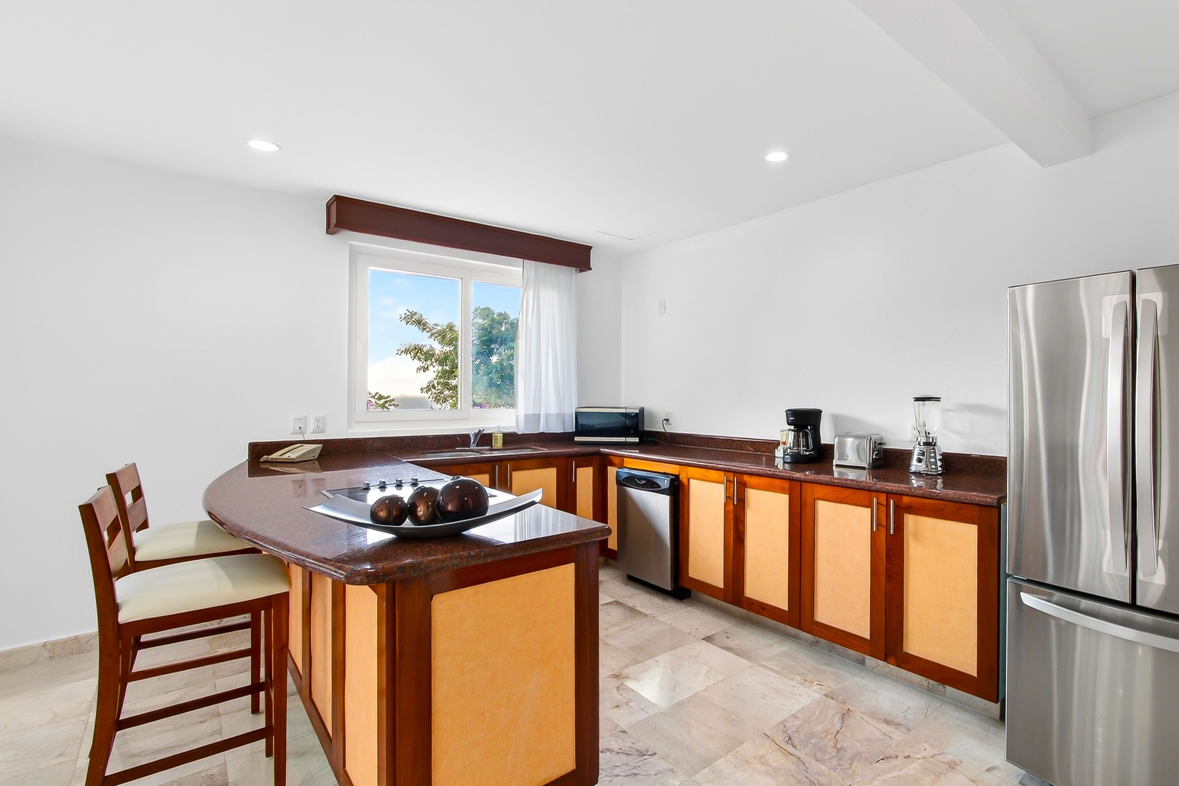 A modern kitchen with a central island, wooden cabinets, stainless steel appliances, and a window providing natural light.