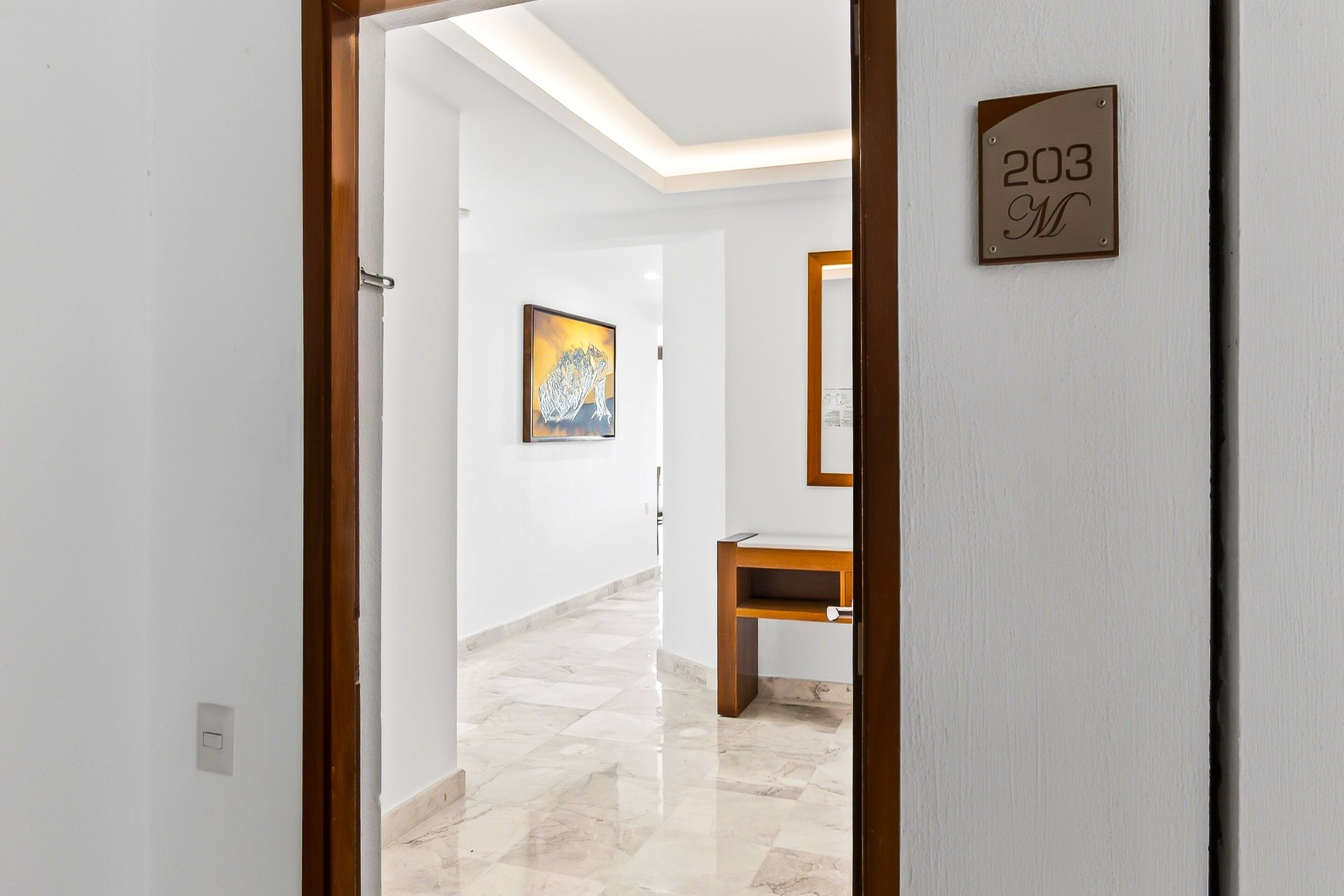 A hallway with a wooden door, a number sign, a painting, and a wooden bench.