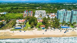 An aerial view of a coastal resort with beachfront villas, a pool, and a beach area. - Ocean-view Condo With Resort Pool & Sundeck (Nuevo Nayarit)