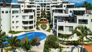 A modern hotel with multiple floors, a central courtyard with a swimming pool, and surrounding greenery. - Ocean-view Condo With Resort Pool & Sundeck (Nuevo Nayarit)
