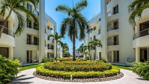 A multi-story hotel with a central courtyard featuring palm trees and well-maintained landscaping. - Ocean-view Condo With Resort Pool & Sundeck (Nuevo Nayarit)