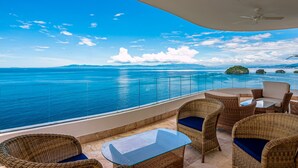Ein Balkon mit Korbmöbeln, einem Glastisch und Blick aufs Meer.
