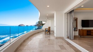 Ein Balkon mit Meerblick, ein Holzstuhl und ein Fernseher in einem Zimmer.