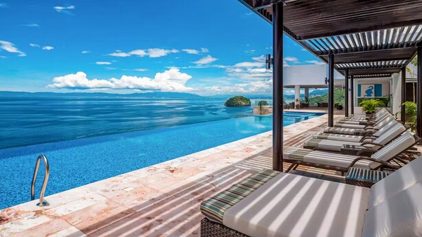 Ein Infinity-Pool mit Liegestühlen und einer Pergola mit Blick aufs Meer.