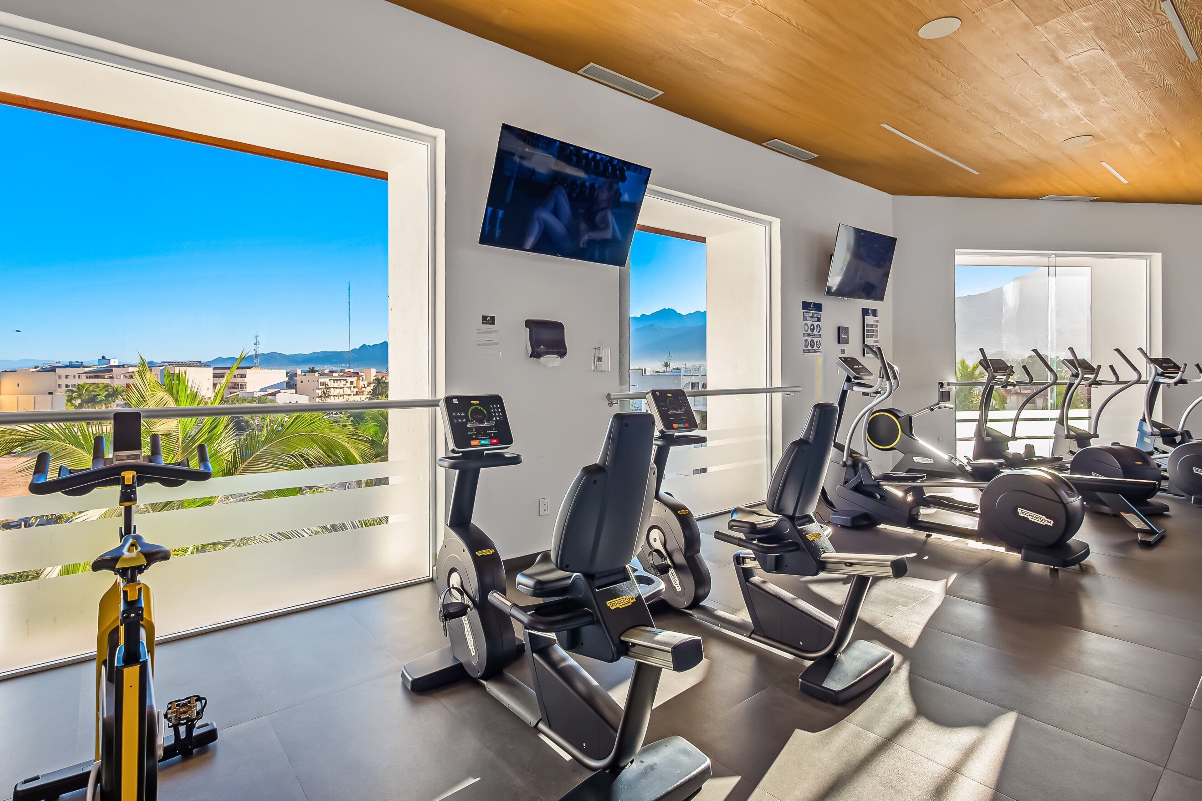 A gym with exercise equipment, large windows, and a view of the city.