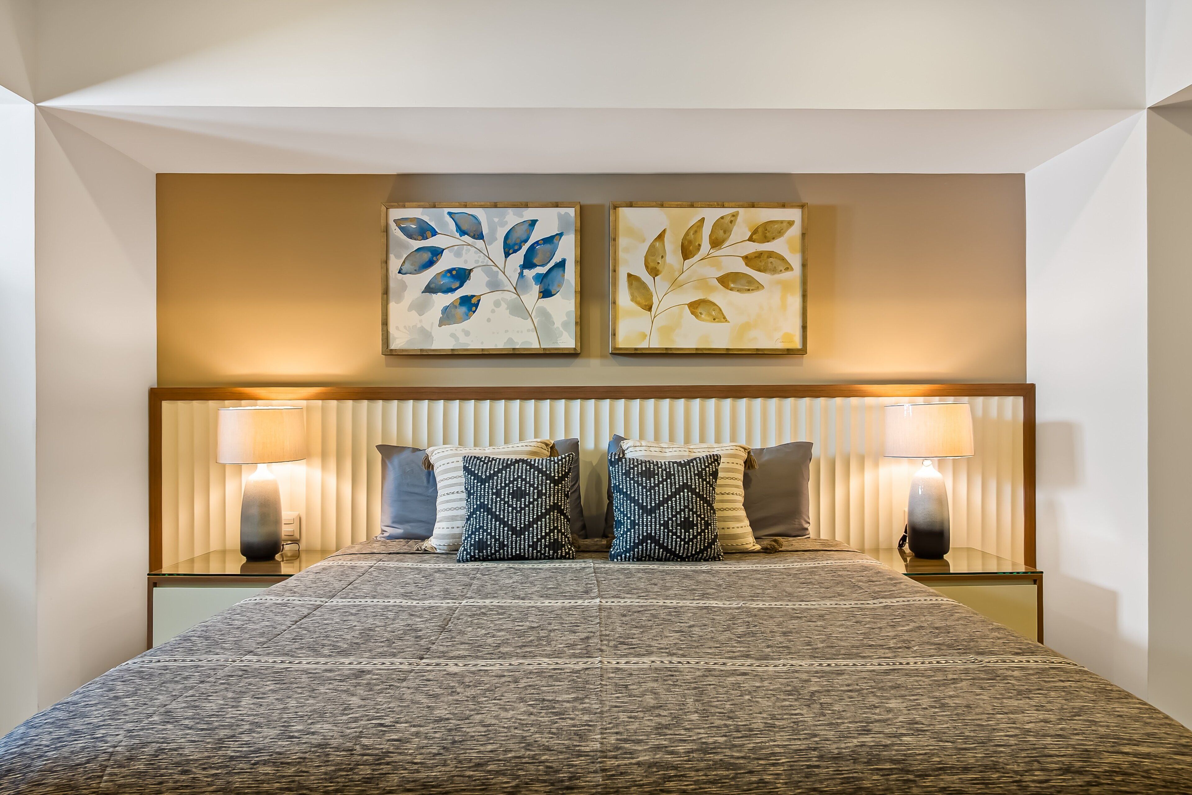 A neatly arranged hotel room with a bed, two bedside lamps, a headboard, and two wall-mounted artworks.