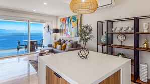 A modern living room with a large island, a dining area, and a view of the sea. - Luxury Oceanfront Apartment With Private Balcony, Rooftop Pool & gym Access (Puerto Vallarta)