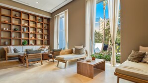 A modern living room with a sofa, a wooden bench, a coffee table, and a bookshelf filled with decorative items. - Luxury Oceanfront Apartment With Private Balcony, Rooftop Pool & gym Access (Puerto Vallarta)