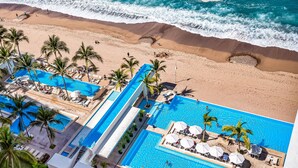 A resort with a large pool, beach access, and palm trees. - Luxury Oceanfront Apartment With Private Balcony, Rooftop Pool & gym Access (Puerto Vallarta)