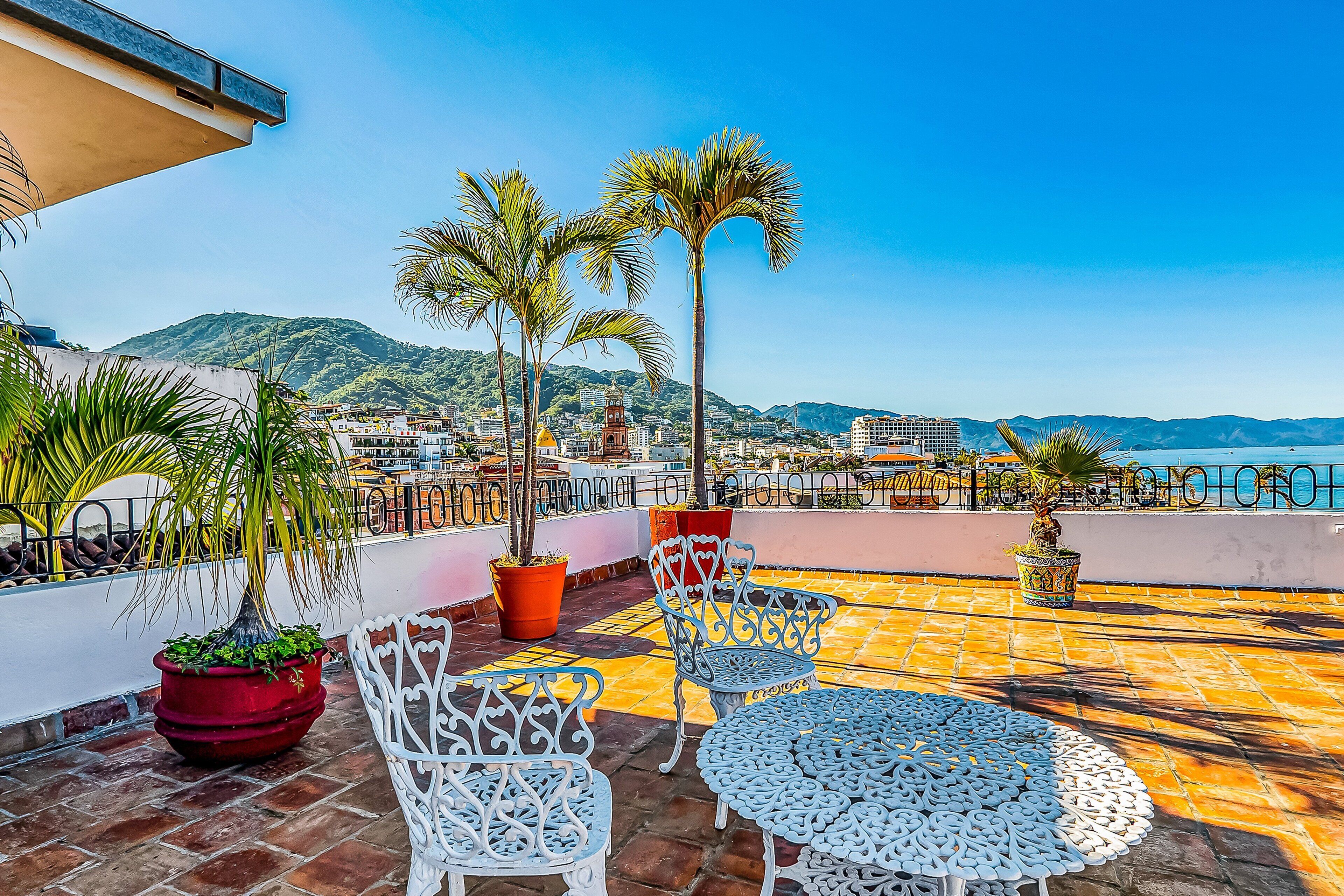 A terrace with outdoor furniture, potted plants, and a view of the city and mountains.