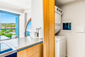 Eine moderne Küche mit integriertem Kaffeeautomat, einer Waschmaschine und Blick auf eine Küstenstadt.