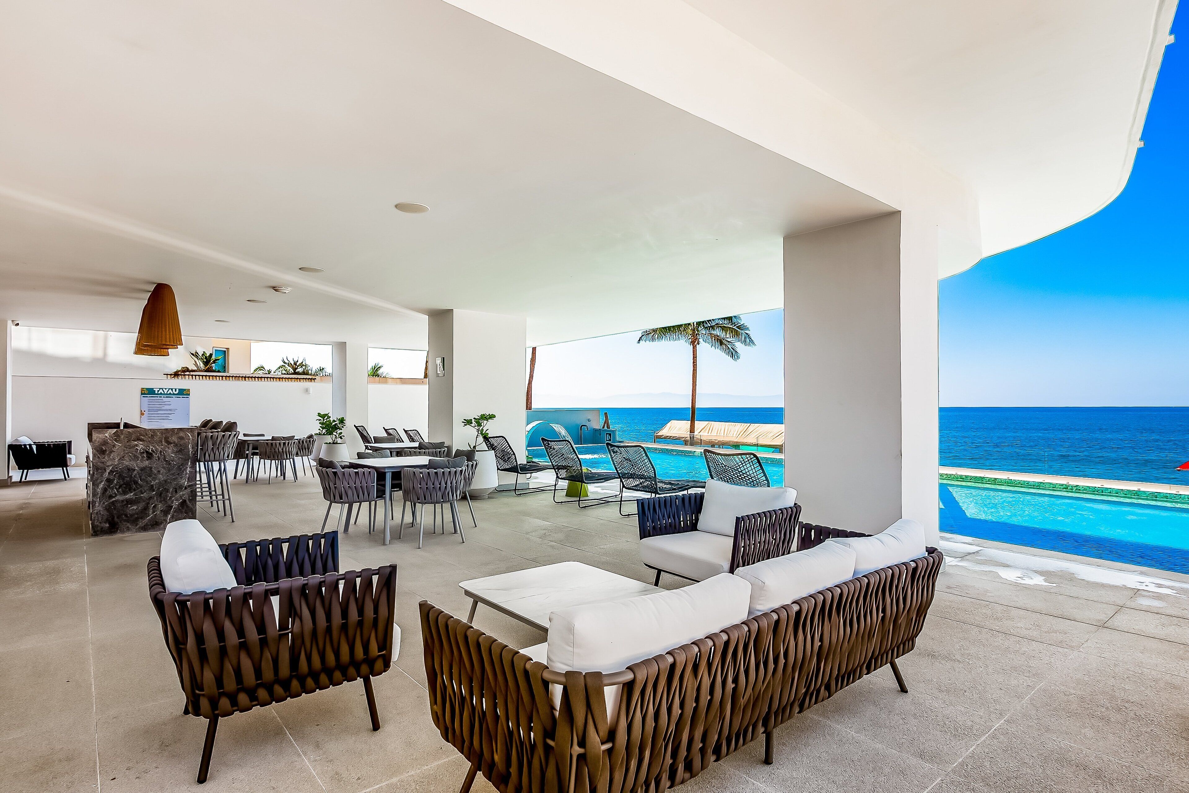 Un área de estar moderna con piscina, mobiliario exterior y vistas al océano.