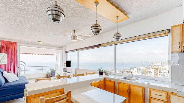 A modern kitchen with a large window, wooden cabinets, and a dining area. - Central Puerto Vallarta Condo With Pool, Ocean Views & Fast Wifi - Walk to Beach (Puerto Vallarta)
