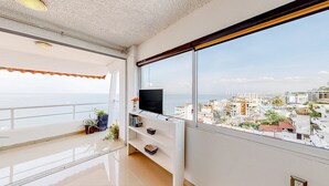 A balcony with a TV, potted plants, and a city view. - Central Puerto Vallarta Condo With Pool, Ocean Views & Fast Wifi - Walk to Beach (Puerto Vallarta)