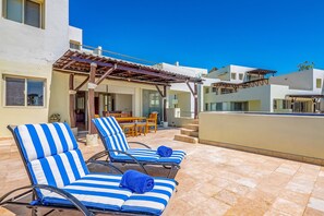 Eine Dachterrasse mit blau gestreiften Liegestühlen und einer Pergola.