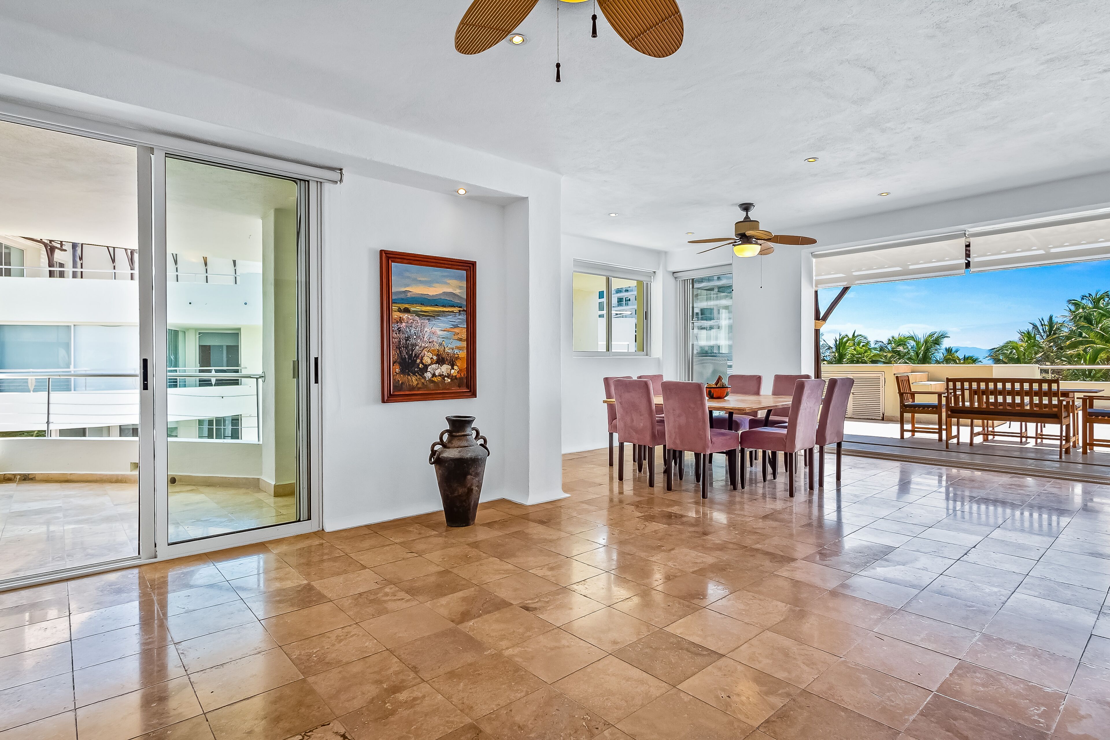 A spacious dining area with a large table and chairs, a ceiling fan, and a view of the outdoors.