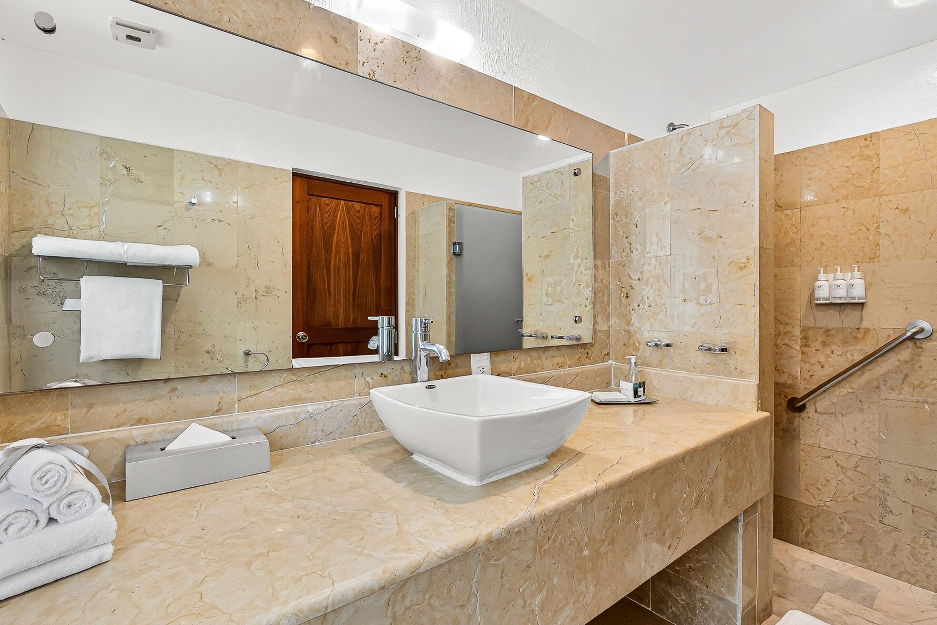 Un bagno moderno con un ampio specchio, un lavabo sospeso bianco, un porta asciugamani e una zona doccia.