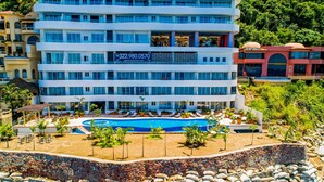A multi-story hotel with a swimming pool, surrounded by rocks and palm trees. - Exceptional Waterfront Condo With Pool, Balcony, Fitness Area, & W/D (Puerto Vallarta)
