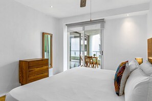A bedroom with a large bed, a wooden dresser, a dining table with chairs, and a sliding glass door leading to a balcony. - Bright Coastal Apartment With Pool, Balcony & Beach Access Close by (Nuevo Nayarit)