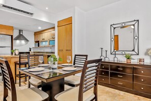 A modern kitchen with wooden cabinets, a dining table set for four, and a large mirror on the wall. - Ocean-view Condo With Pools, Roof Deck, Lounge, Private Balcony, & AC (Nuevo Nayarit)