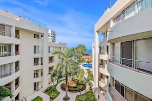 A multi-story hotel with balconies, a central courtyard with palm trees, and a pool in the background. - Ocean-view Condo With Pools, Roof Deck, Lounge, Private Balcony, & AC (Nuevo Nayarit)