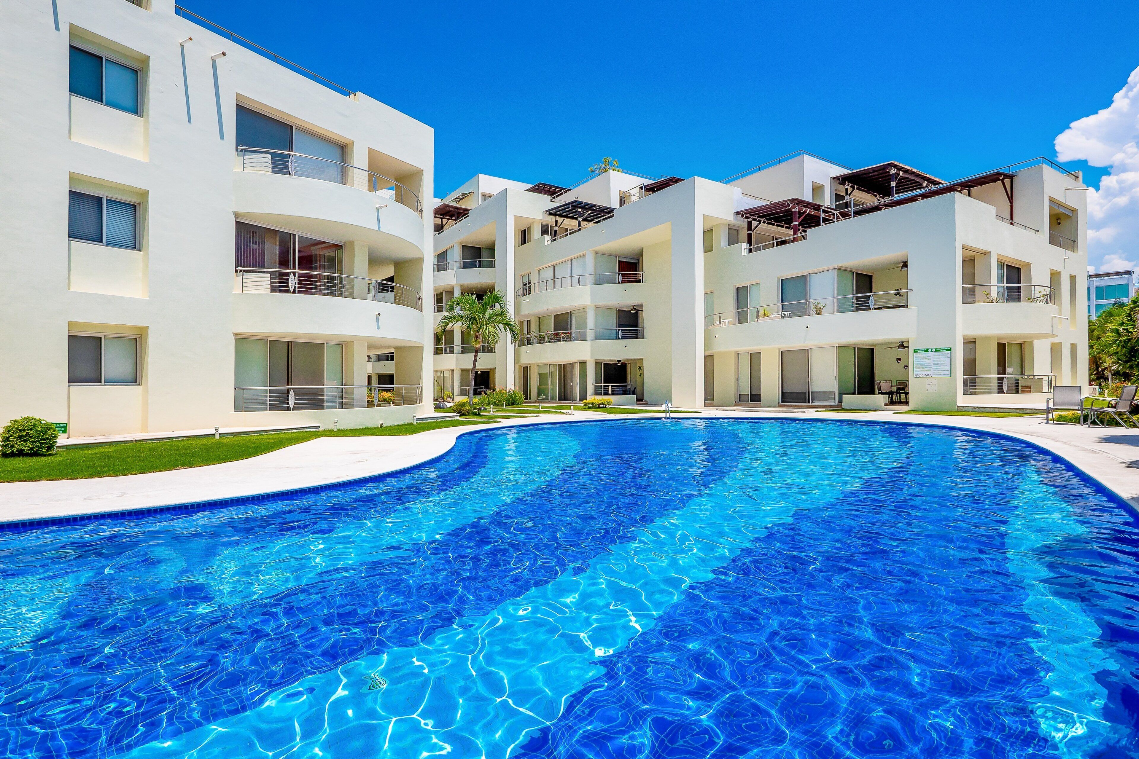 Un hôtel moderne doté d’une piscine, de nombreux balcons et offrant une vue sur un ciel d’un bleu éclatant.