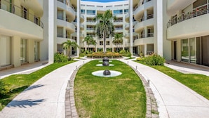 Un edificio moderno de varios pisos con un patio central, palmeras y una fuente.