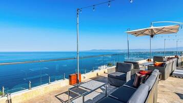 Une terrasse sur le toit, dotée d’un espace extérieur aménagé, d’une balustrade en verre et offrant une vue sur la mer.