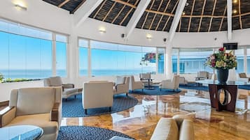En rymlig entréhall med högt i tak, stora fönster med utsikt över havet och ett centralt område med sittplatser och en dekorativ vas.