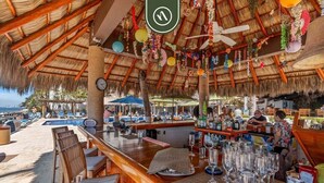 Un bar situé en bord de mer, doté d’un toit de chaume, de tables en plein air et offrant une vue sur l’océan.