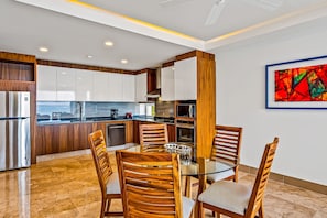 A modern kitchen with white cabinets, wooden accents, and a dining area with a glass table and wooden chairs. - Luxe 8th-floor Condo With Endless Ocean Views, Pool, spa & Balcony (Puerto Vallarta)